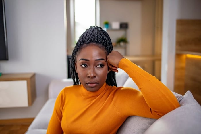 A person looking stressed and thoughtful while sitting on their couch.