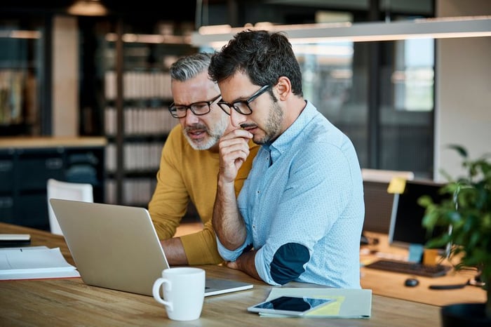 Two men in thought looking at a laptop screen together.