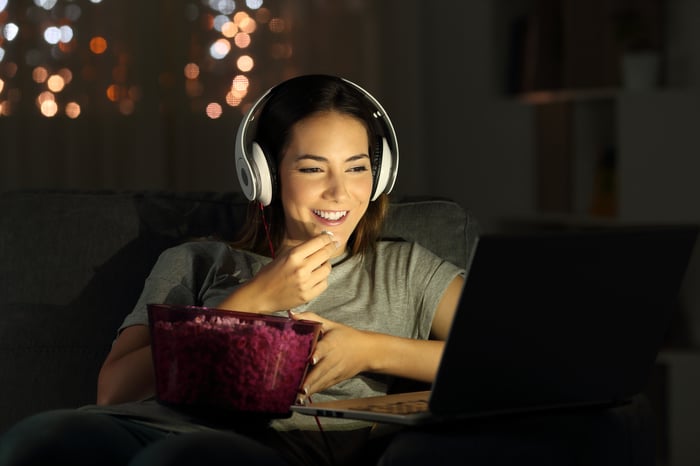 A person eats popcorn while watching a movie on a laptop computer.