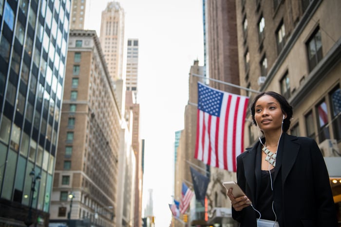 A person holding a smartphone stands on a city street.