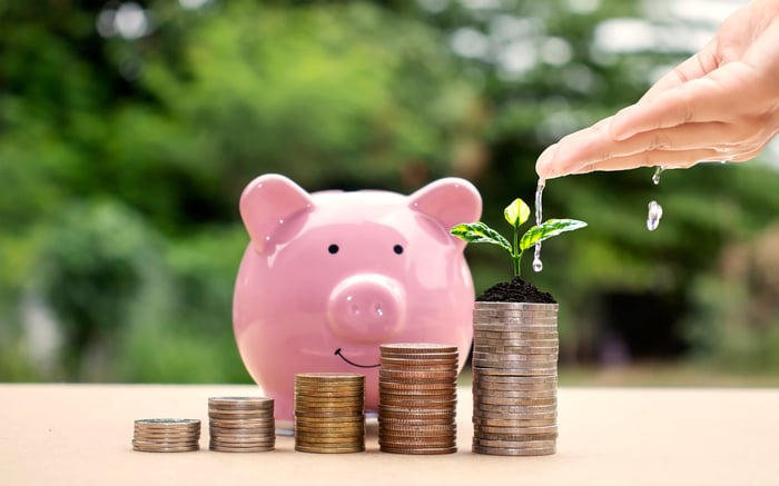 A piggy bank with stacks of money and a hand putting water on them, showing growth.