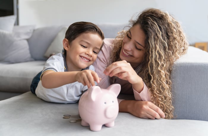 A smiling parent and their child put coins in a piggy bank.