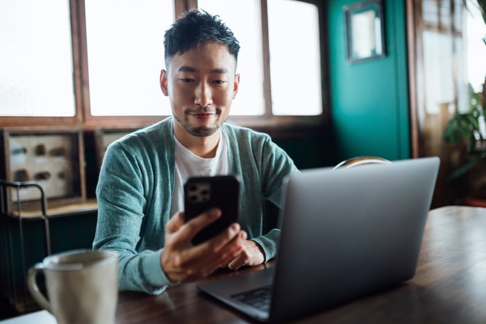 Investor with laptop looking at smartphone.