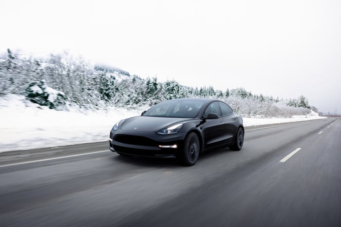 A Tesla Model 3 driving down a wintry road. 