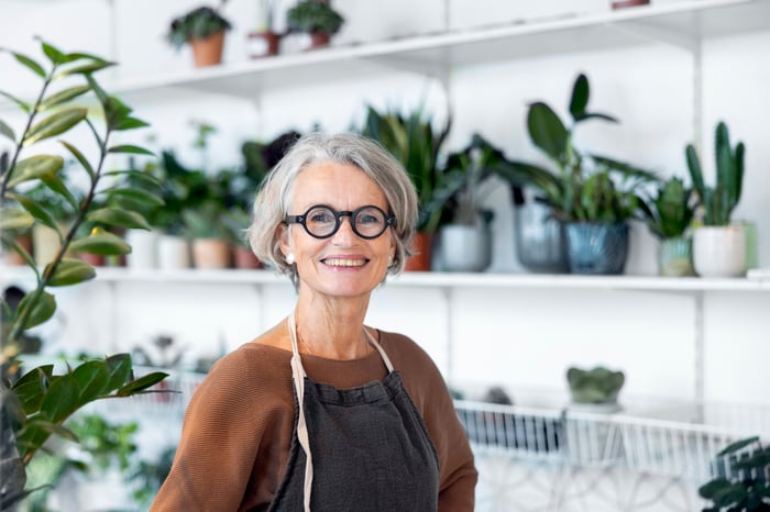 A smiling person standing in front of green plants.