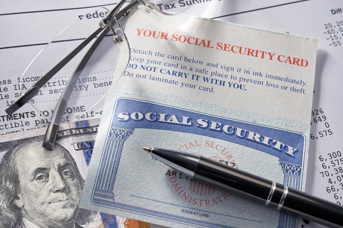 A Social Security card sitting atop a $100 bill and paper documents.