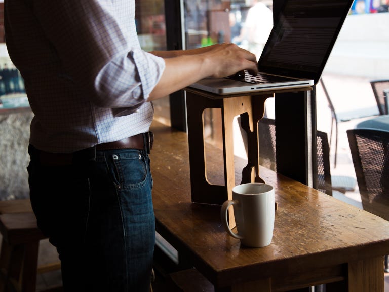 A man using a StandStand desk converter at a coffee shop.