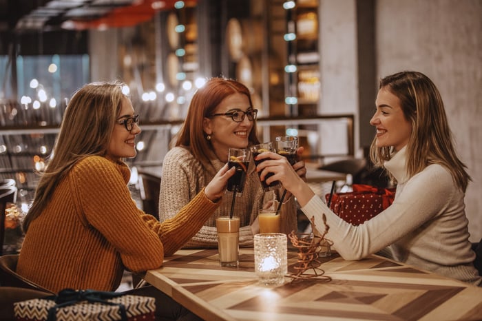 Three friends raise their glasses in a toast in a restaurant.