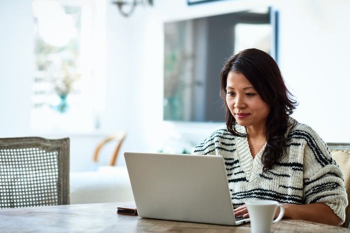 A woman sitting at her dining table and typing on her laptop.