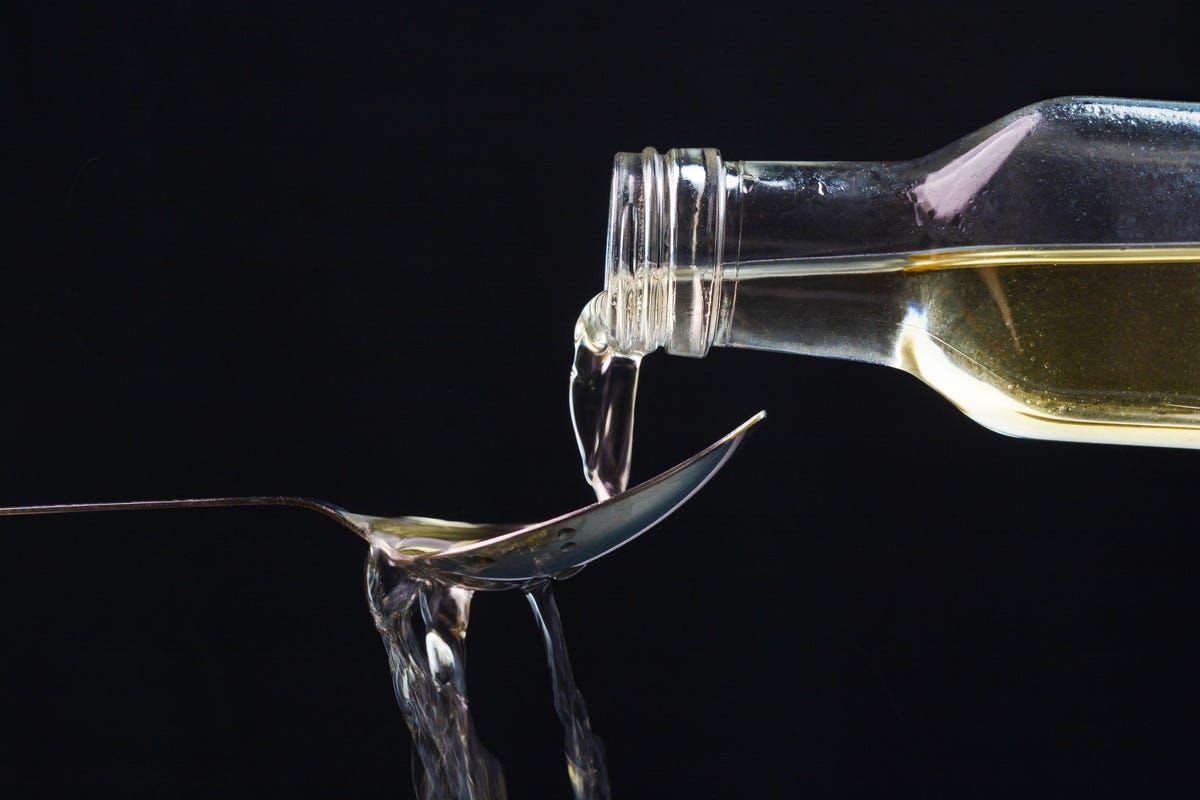 A bottle of apple cider vinegar pouring over a spoon