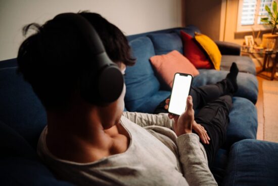 Young man sitting on a couch with headphones on scrolling on his phone