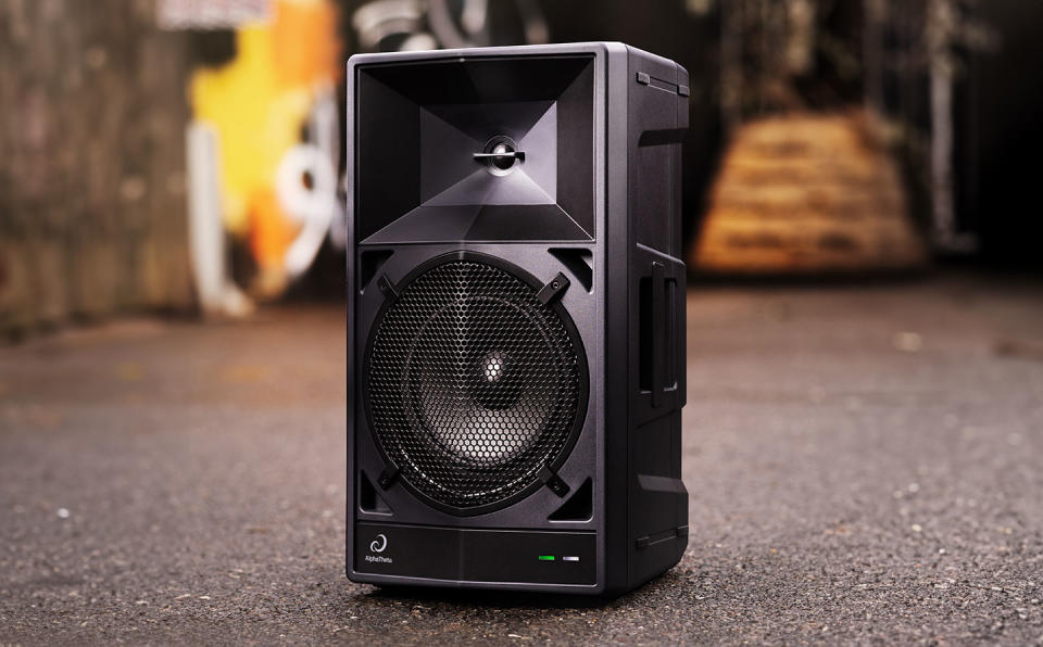 A black AlphaTheta Wave-Eight loudspeaker sits in the middle of a paved backyard area.