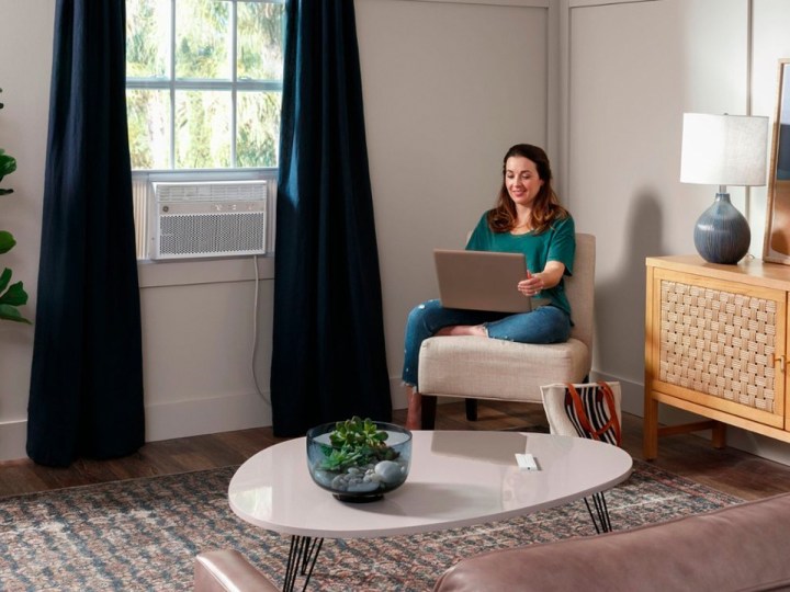 A woman works on a laptop as a GE 8,000 BTU smart window air conditioner cools the room.