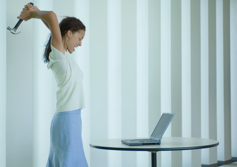 Woman about to swing a hammer at a laptop.