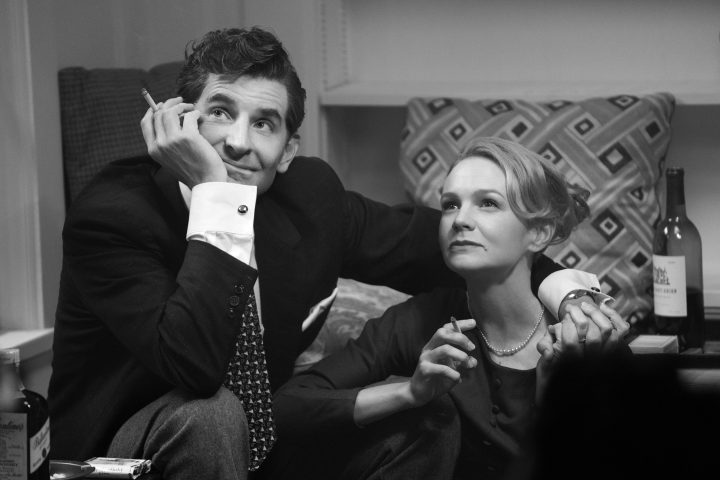 A man and woman sit next to each other while smoking a cigarette.