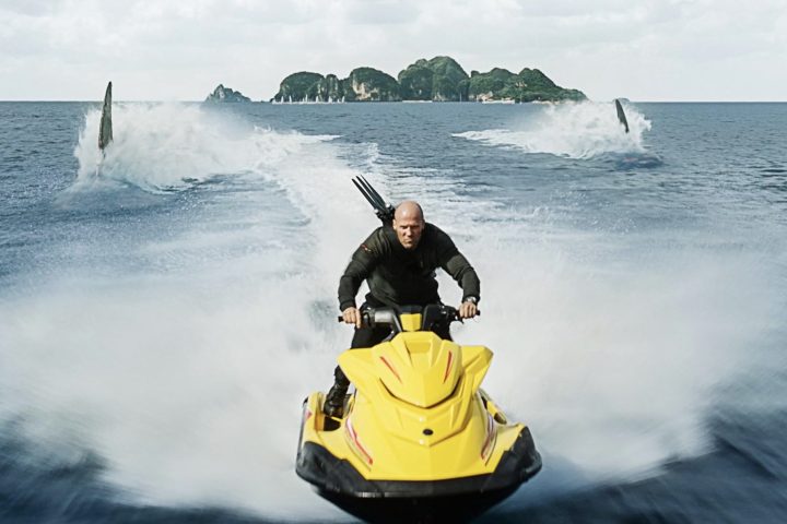 A man rides a jet ski in front of two sharks.