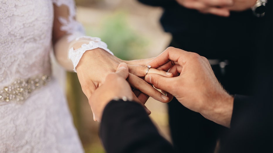 Groom puts wedding band on bride's finger.