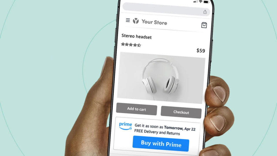 Promotional image for Amazon's Buy with Prime program. Closeup of a hand holding a phone with a Buy with Prime button highlighted in blue (on a generic headphone buying screen).