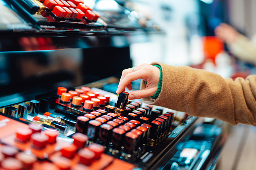 Close-up of young woman choosing lipstick at cosmetic counter in the shop