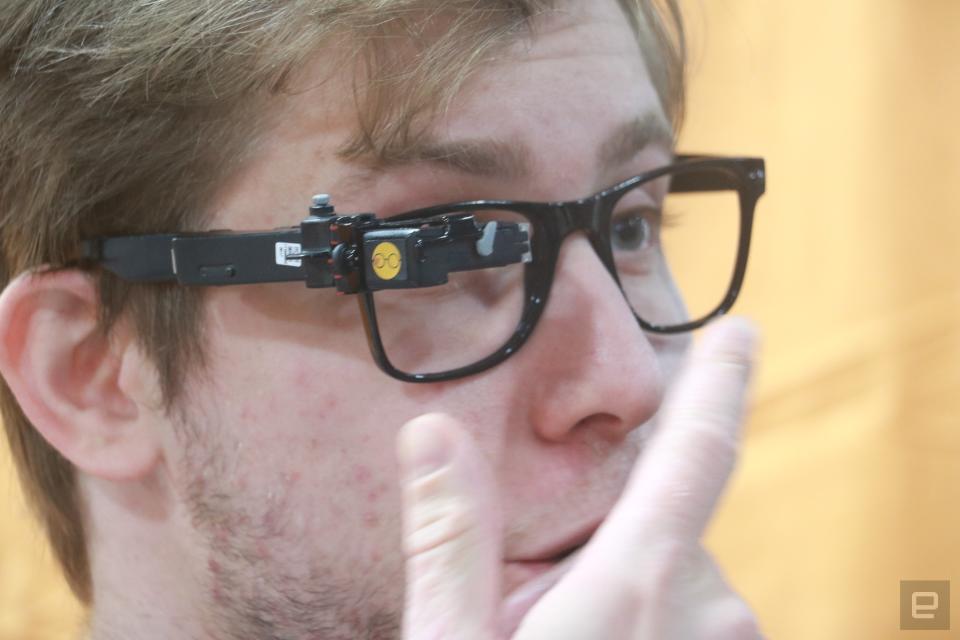 A person wearing the TranscribeGlass on the right side of a pair of black-framed glasses. 