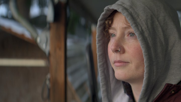 A young woman with a hoodie looks off to the distance in a scene from Escaping Twin Flames.