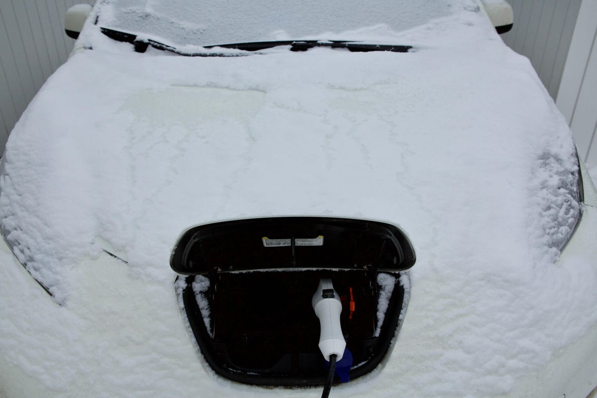 snow-covered electric car with its charging point open and charger plugged in