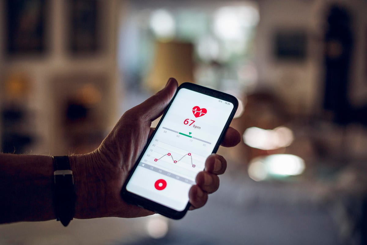 A hand holds a phone with heart rate tracking.