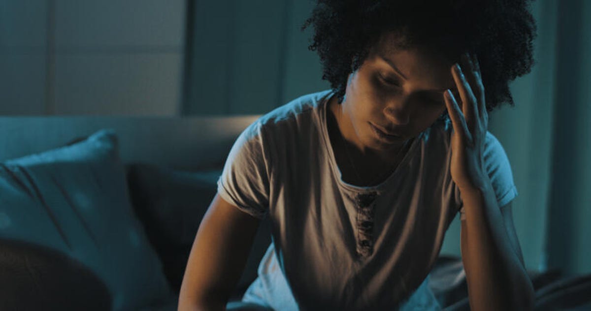 Woman sitting on the edge of her bed with her head in her hand because she can't sleep.