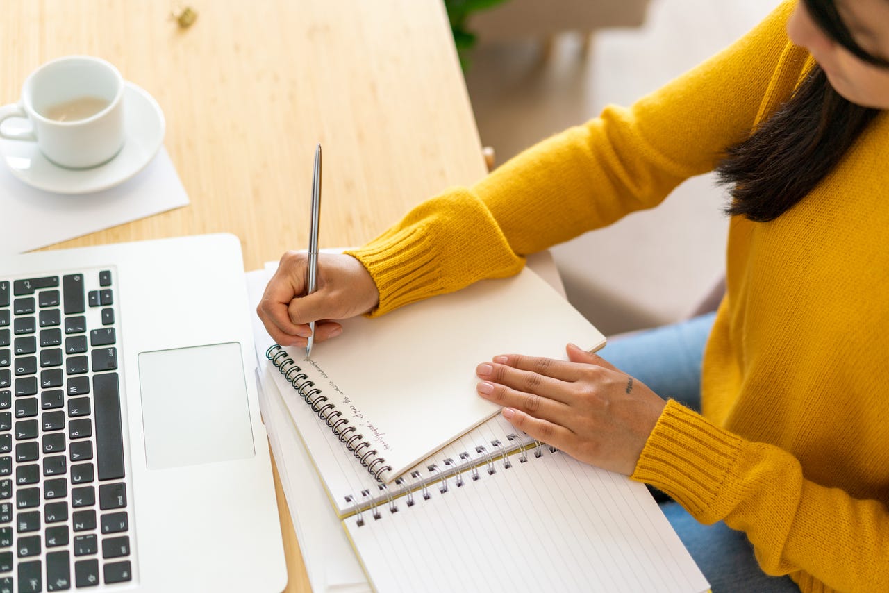 Person writing notes with laptop open