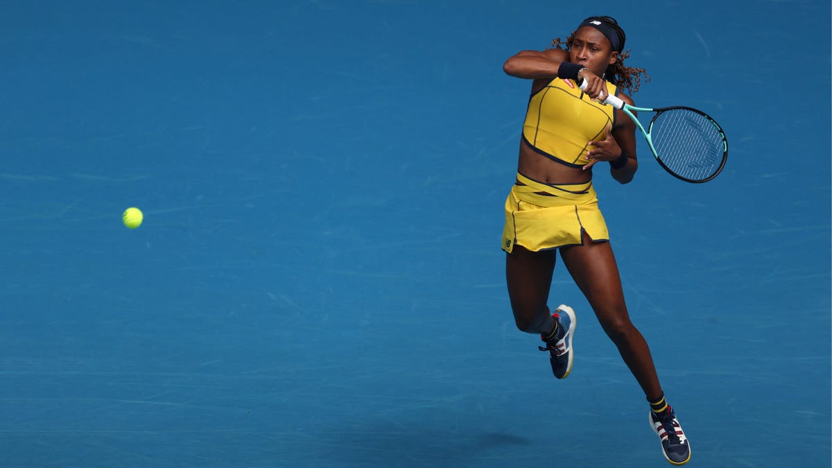 Tennis player Coco Gauff hits a return, playing on blue hard court surface.