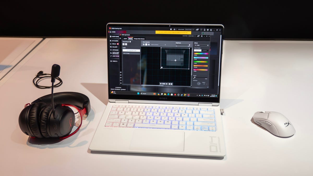 HP Omen Transcend 14 gaming laptop open facing front on a white table with a black background with a white HyperX gaming mouse to the right and a black-and-red HyperX wireless gaming headset to the left.