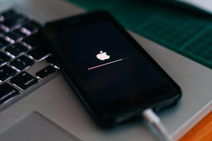 iPhone plugged in atop MacBook showing Apple logo during a software update recovery.