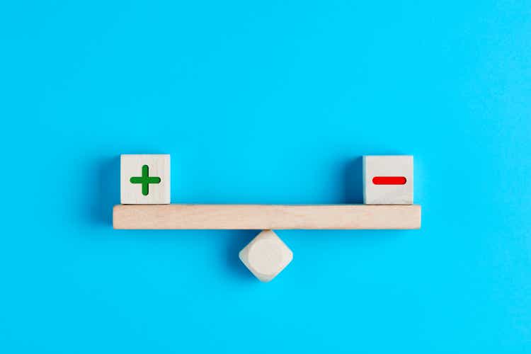 Plus and minus or positive and negative symbols on wooden blocks are in balance on a wooden seesaw