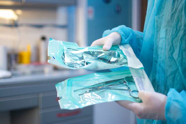 Close up of dentist hands in white sterile gloves holding dental tools for surgical use packed in a protective foil at dental office