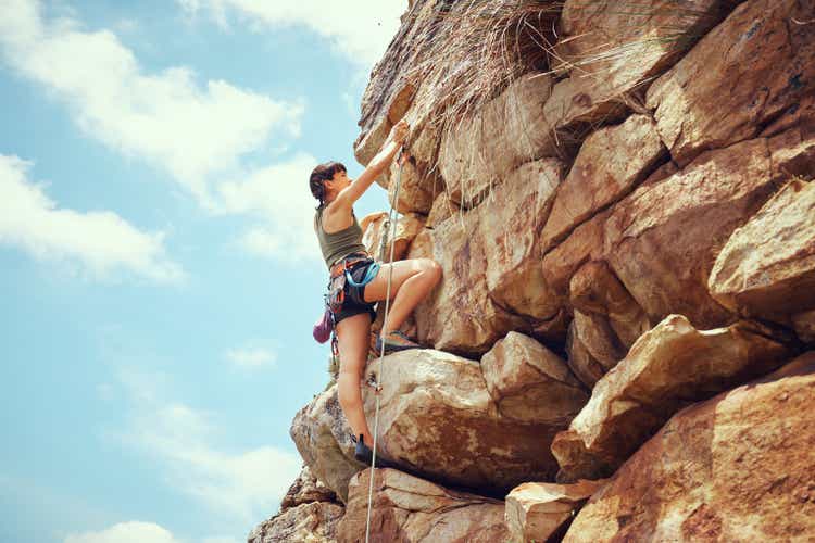 A woman in nature rock climbing, training and fitness outdoors on a sunny day with climbing equipment. A female, strong and healthy athlete doing exercise, physical activity and extreme climbing.