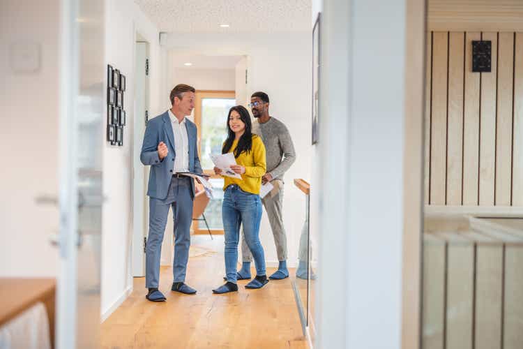 Adult Caucasian Male Real Estate Agent Selling And Showing The Modern Apartment To His Diverse Young Clients That Are Standing Next To Him In The Fancy Apartment