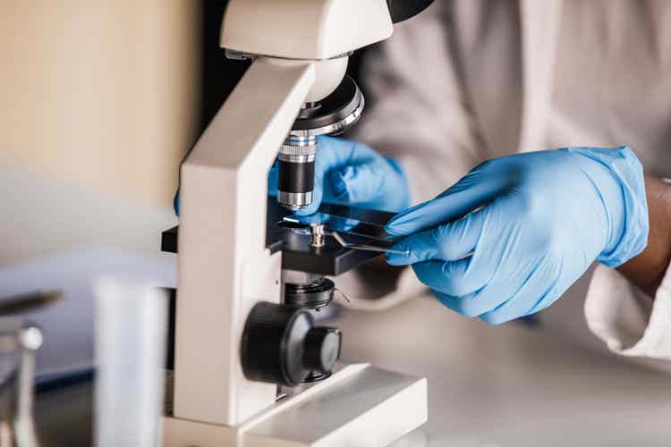 Lab tech in protective gloves putting a slide with a scientific sample under a microscope