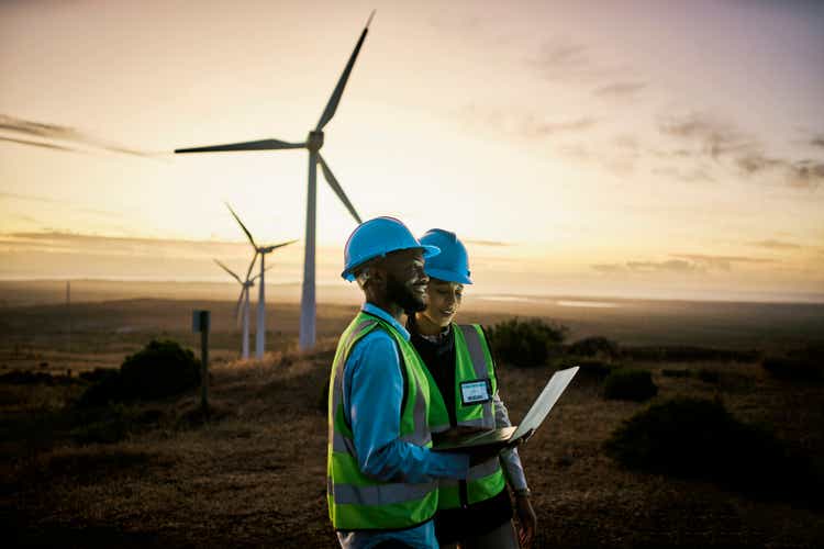 Laptop, farm and engineer team together at night for renewable energy, power and wind turbine. Electrician or technician man and woman in nature for electricity, eco and green environment maintenance