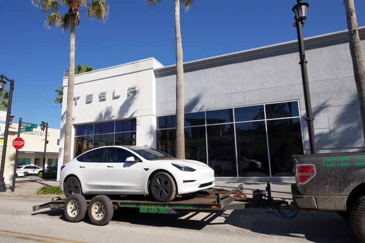 Trailer carrying Tesla car parked in front of Tesla building