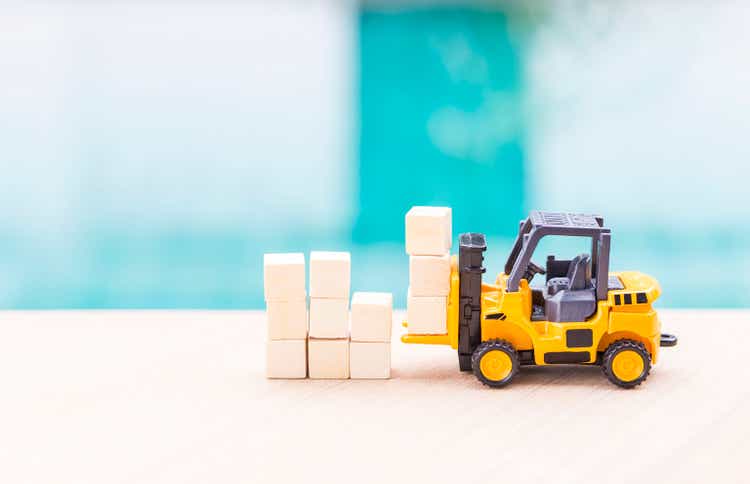 Miniature worker in safety suite on forklift truck and wooden cubes