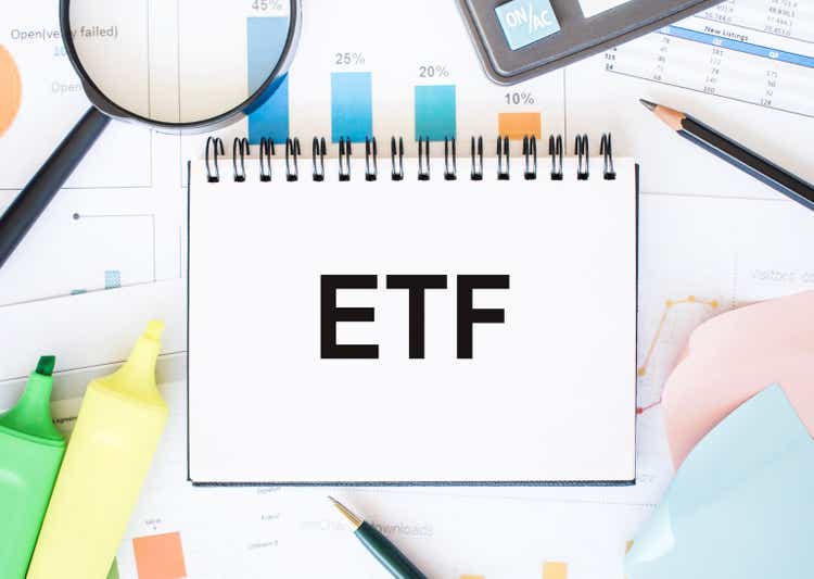 On the table are reports, diagrams, a pen, a magnifying glass and a white notepad with text ETF Exchange Traded Funds. Business concept