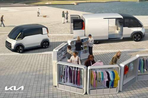 A small white mini van sits side by side a much larger mini van. In the foreground is a group of people shopping at a pop-up clothing stand.