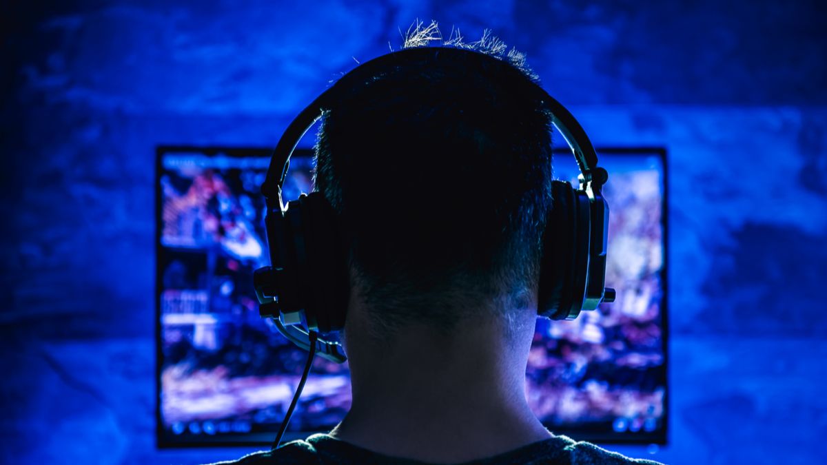 Back of a man's head as he's gaming late at night with wired headphones on.