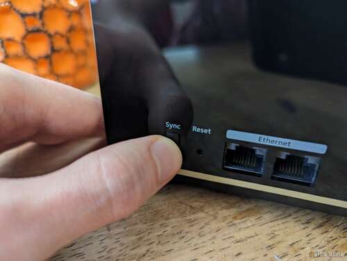 Person's thumb pushing the sync button the back of a Netgear Nighthawk MK93S mesh node.