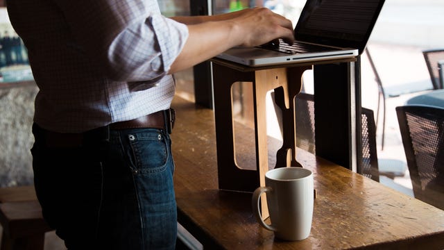 A man using a StandStand desk converter at a coffee shop.