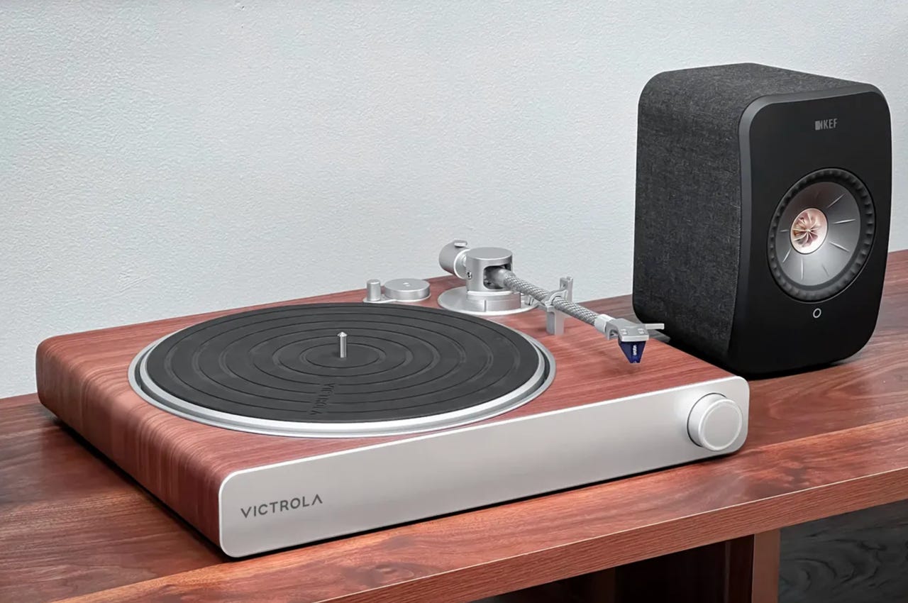 Victrola record player on a wooden table next to a black bookshelf speaker