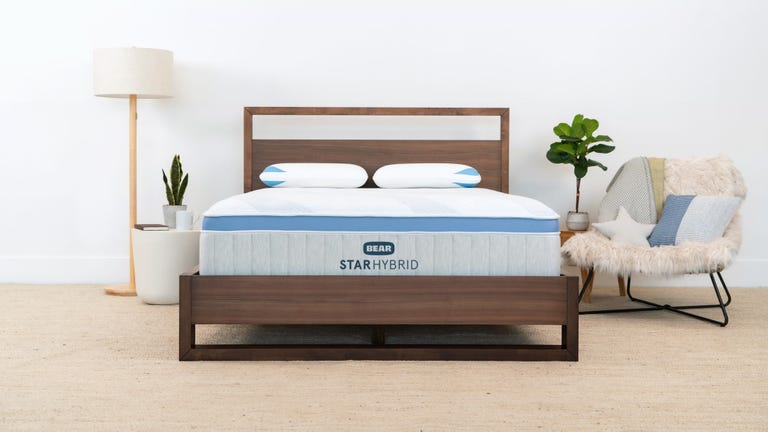 The Star Hybrid mattress from Bear on a wooden bed frame next to a lamp and chair.