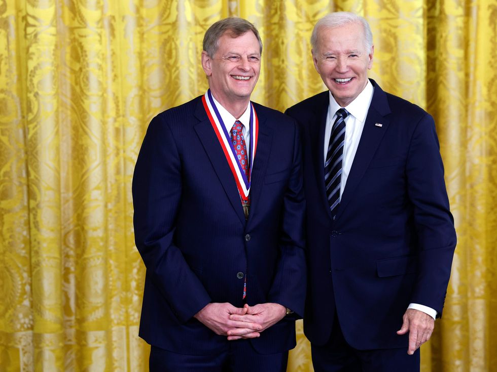 two men standing smiling for the camera in suits against a yellow background