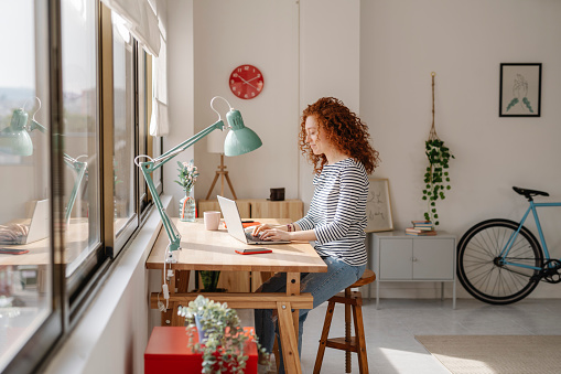 Woman sitting on a desk using a laptop computer while working from home.