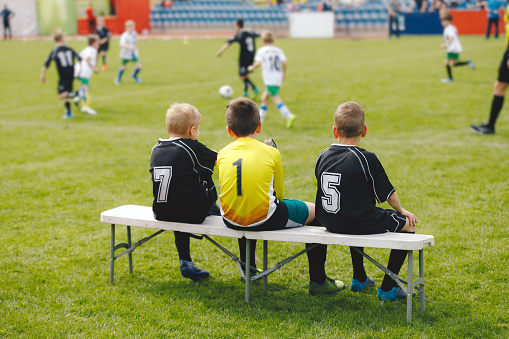 Young boys in soccer jerseys sitting on the substitute players